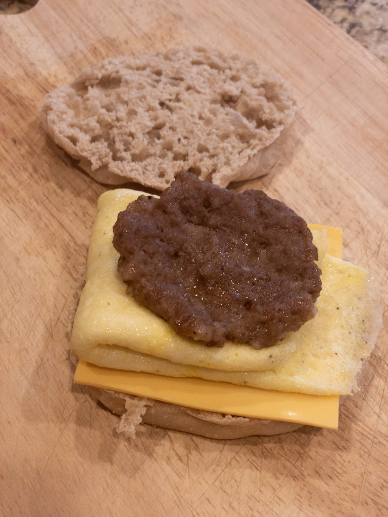 Layer cheese, egg, and sausage between the top and bottom of the English muffin 